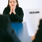 Woman in a serious job interview with resume in focus, sitting at a table.